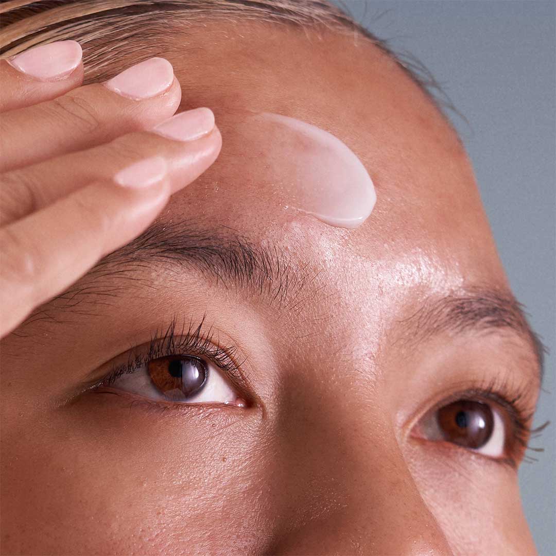 Eine Person trägt mit den Fingern einen Klecks der weißen Creme Collagen Preservation Duo auf die Stirn auf und konzentriert sich dabei auf Feuchtigkeit und Hautpflege, um Hautalterung vorzubeugen.