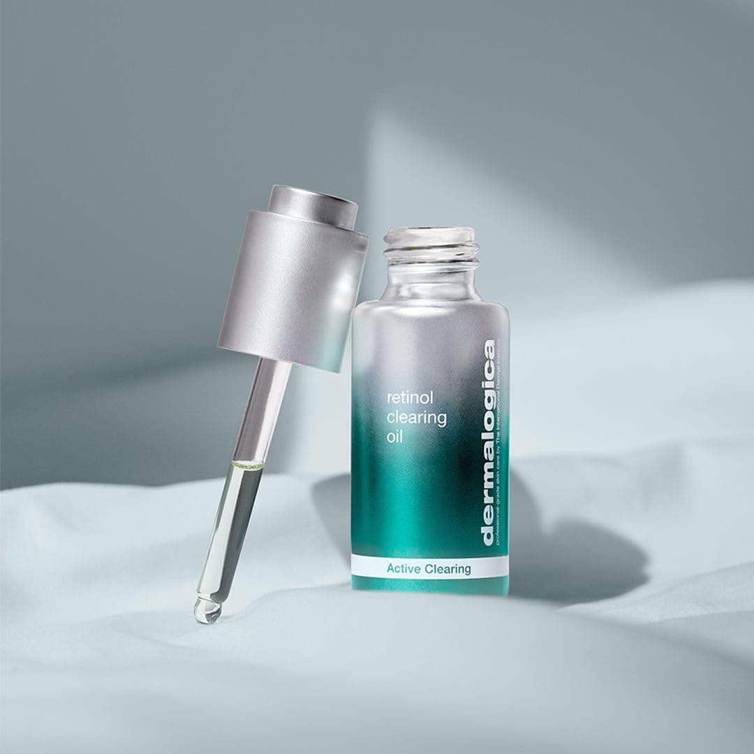 Eine Flasche Retinol Clearing Oil mit einer Pipette, präsentiert auf einem hellblauen Stoffhintergrund.