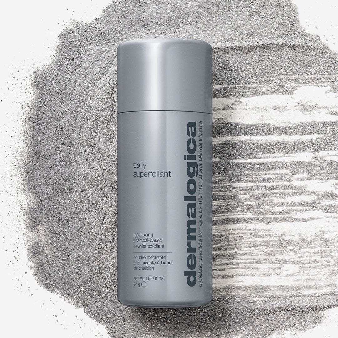 Vor einem hellen Hintergrund steht eine Flasche Daily Superfoliant auf einem verstreuten Haufen grauen Pulvers, das mit Binchotan-Aktivkohle angereichert ist.