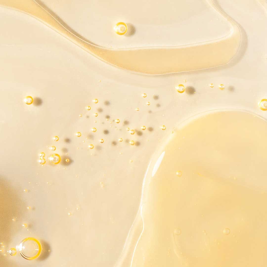 Nahaufnahme eines viskosen, hellgelben Phyto Nature Firming Serums mit kleinen und großen Bläschen auf einer glatten Oberfläche, angereichert mit biomimetischen Peptiden zur Bekämpfung von Zeichen der Hautalterung.