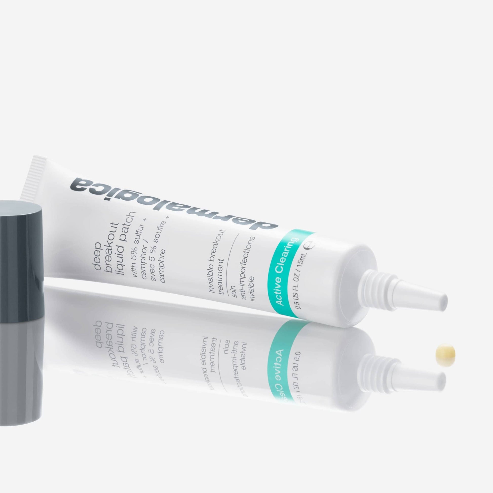 Eine weiße Tube Deep Breakout Liquid Patch mit einer grauen Kappe liegt auf einer weißen Fläche; ein kleiner beiger Tupfer dieses veganen Hautpflege Schwefel Spot-Treatment befindet sich in der Nähe der Applikatorspitze.