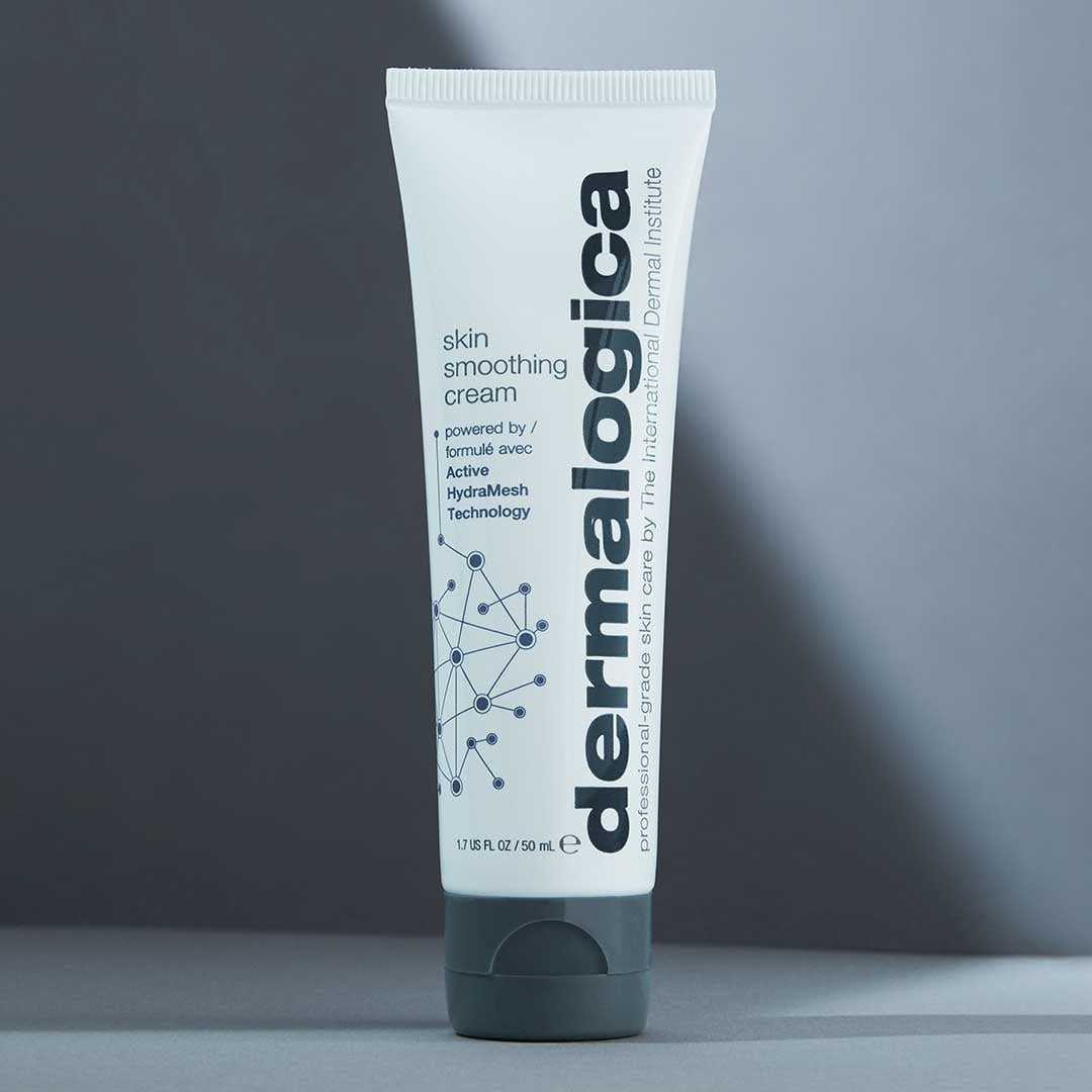 Eine Tube der Skin Smoothing Cream mit weißem und grauem Design und der feuchtigkeitsspendenden HydraMesh Technologie™ steht aufrecht auf einer grauen Fläche.