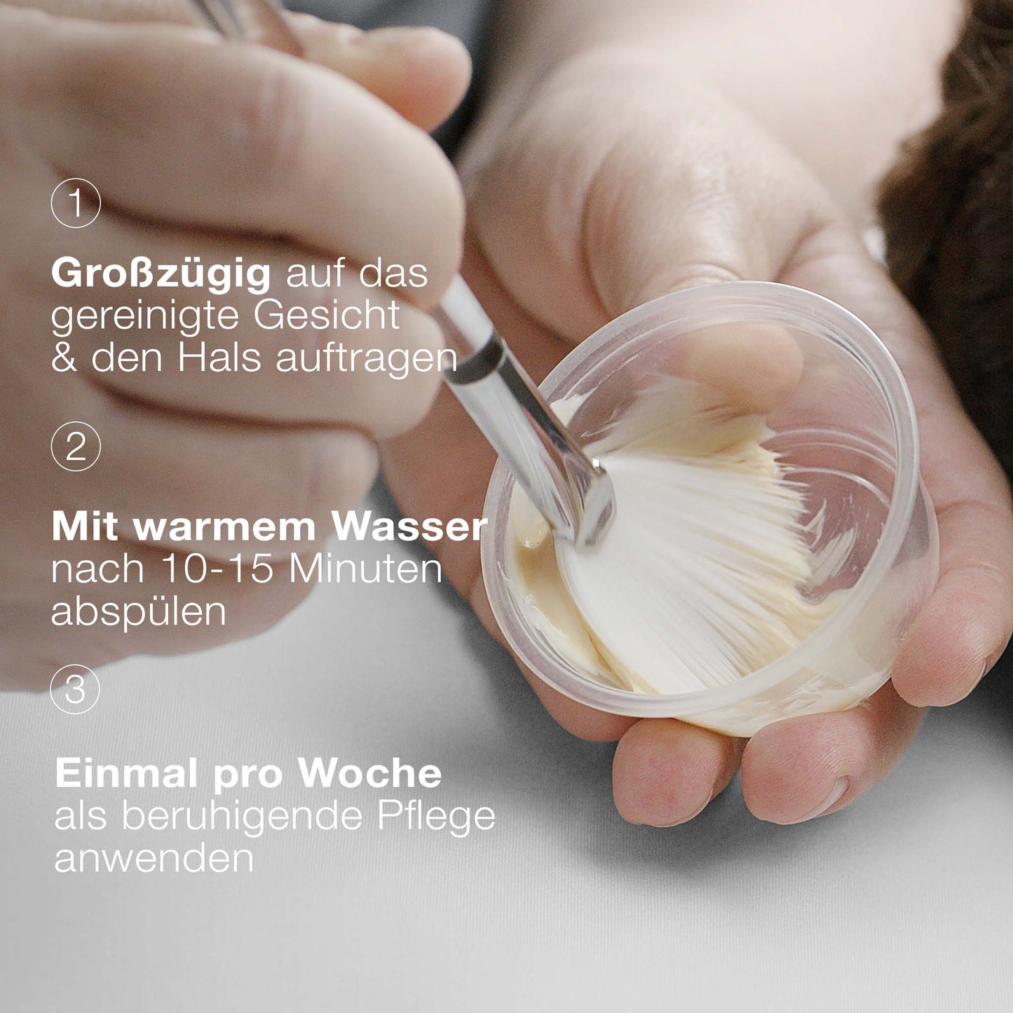 Eine Hand taucht einen Pinsel in einen kleinen Behälter mit MultiVitamin Power Recovery Masque, mit deutschen Anweisungen zum Auftragen und Abspülen der antioxidativen Behandlungsmaske auf der linken Seite.