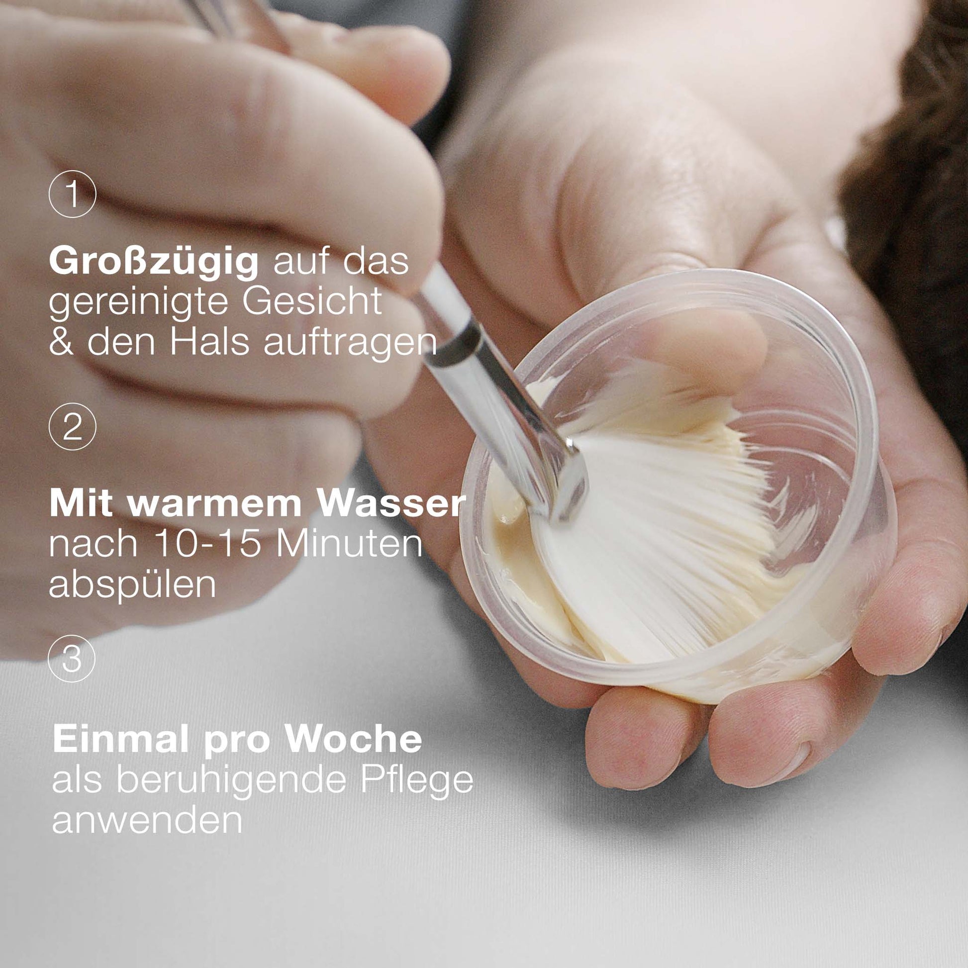 Eine Hand taucht einen Pinsel in einen kleinen Behälter mit MultiVitamin Power Recovery Masque, mit deutschen Anweisungen zum Auftragen und Abspülen der antioxidativen Behandlungsmaske auf der linken Seite.