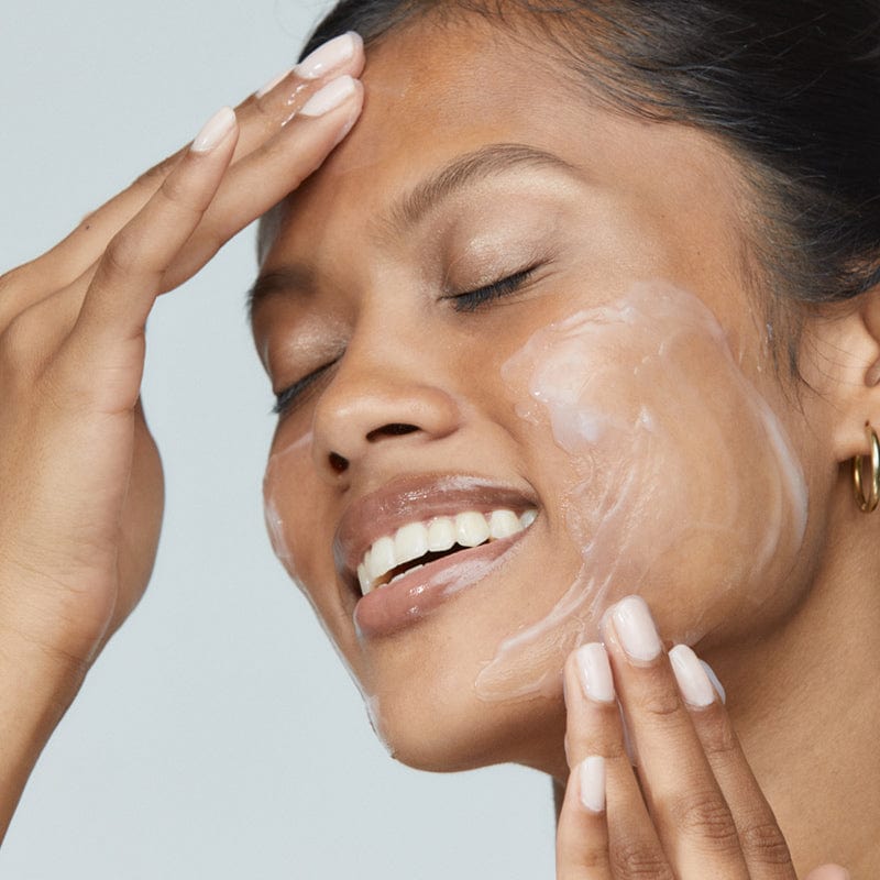 Eine Person mit geschlossenen Augen trägt die Stabilizing Repair Cream + UltraCalming Cleanser sanft auf ihre Wange auf und lächelt dabei - ein beruhigendes Ritual für empfindliche Haut.