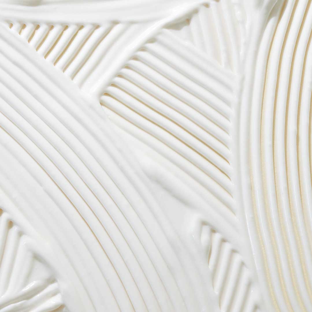 Nahaufnahme einer weißen, cremigen Substanz mit strukturierten, diagonalen Linien und Rillen, die ein geometrisches Muster bilden – Clearing Defense SPF30 ist mit antioxidativen Inhaltsstoffen für verbesserten Hautschutz angereichert.