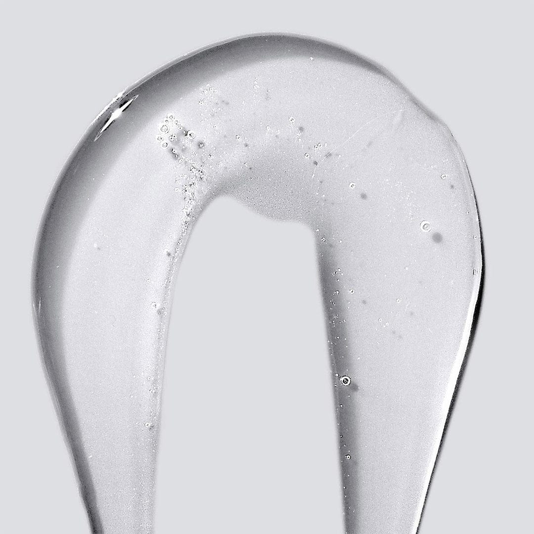 Ein klares, dickflüssiges Gel des Conditioning Body Wash mit Provitamin B5 wird bogenförmig auf einen schlichten grauen Untergrund aufgetragen; in der pflegenden Formel sind kleine Luftbläschen sichtbar.