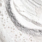 Nahaufnahme eines weißen Pulvers mit einem Ringmuster und verstreuten Flüssigkeitsblasen, das der feinen Textur von Daily Microfoliant ähnelt, einem Produkt zur Verfeinerung des Hautbildes.