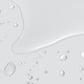 Klare Wassertropfen und eine kleine Pfütze verteilen sich auf einer glatten, hellgrauen Oberfläche und erinnern an die frische Feuchtigkeitsversorgung durch Retinol Clearing Oil.