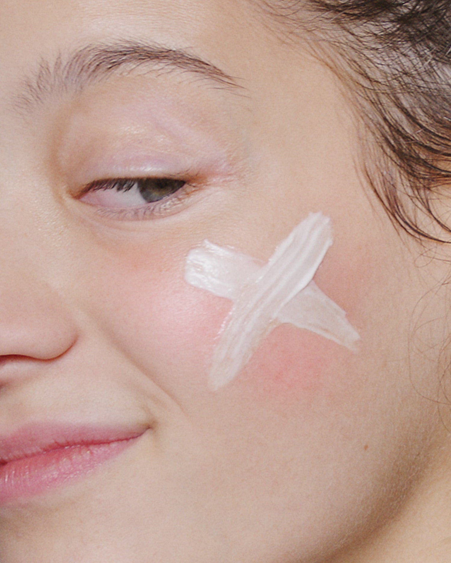 Nahaufnahme des Gesichts einer Person mit einer weißen, X-förmigen Markierung der Stabilizing Repair Cream + UltraCalming Cleanser auf ihrer Wange, ideal für empfindliche Haut.