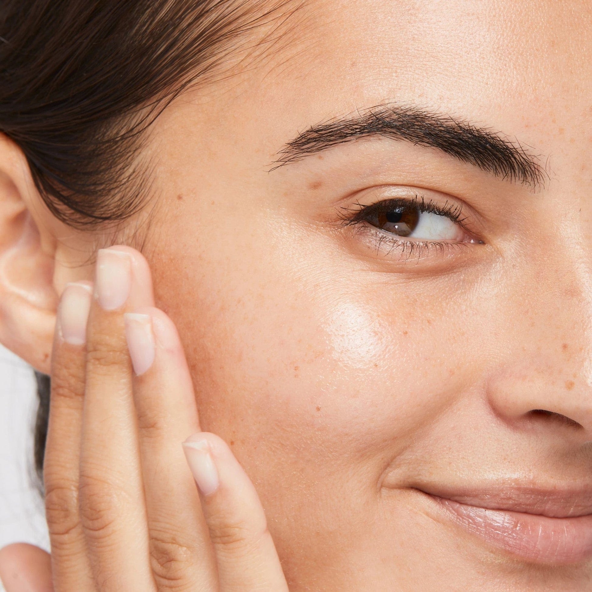 Nahaufnahme des Gesichts einer Person, die sanft ihre eigene Wange berührt. Fokus auf Auge, Wange und Augenbraue.