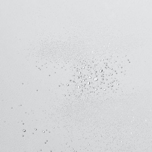 Tropfen klarer Flüssigkeit in verschiedenen Größen auf einer glatten, hellen Oberfläche.